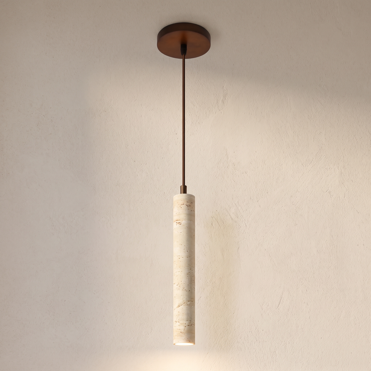 The Anzio slim travertine pendant light hanging against a lime plaster wall, lit from the open lower end