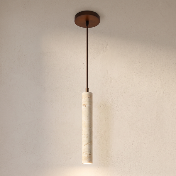 The Anzio slim travertine pendant light hanging against a lime plaster wall, lit from the open lower end