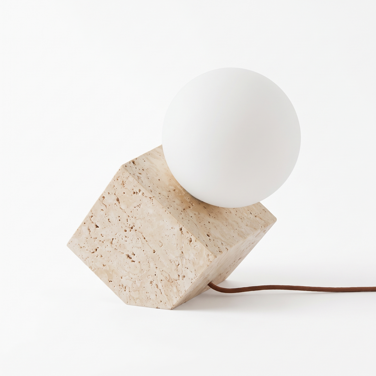 Cortona travertine table lamp, a stone cube tilted on one corner with a frosted opal glass globe in the top face, on a plain white background