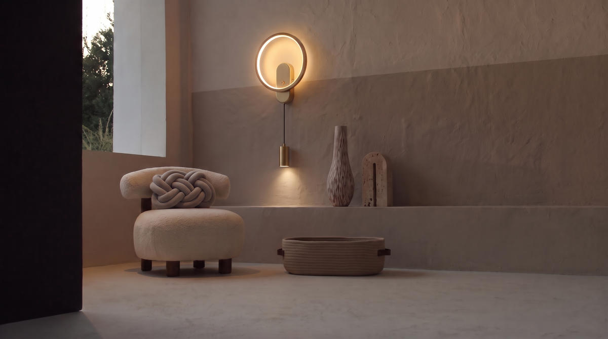 A room at dusk with the Kyoto boucle chair and Oslo knot cushion, the Bergamo ring wall light and its hanging spotlight above a plaster ledge holding the Osaka vase and Milan travertine bookend, and the Helsinki rope basket on the floor