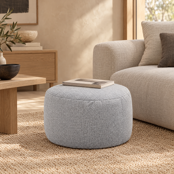 Kumano round floor pouf in light grey on a jute rug beside a linen sofa, book shown for styling only